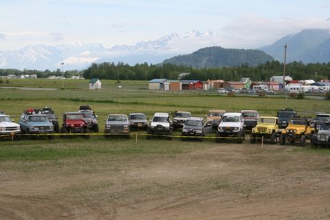 1990 Chevrolet Suburban - A collection of off-road vehicles are parked in a field, with a scenic mountain range visible in the distance.
