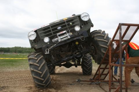 1990 Chevrolet Suburban - A heavily modified truck with oversized tires is positioned on a metal ramp, with a person in safety gear attending to the side.
