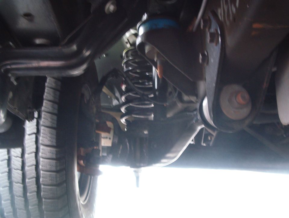 Underbody view of coil-spring rear suspension, differential and driveshaft beneath a vehicle