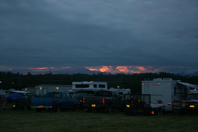 Several pickup trucks and RVs parked in a field at dusk with mountains in the background