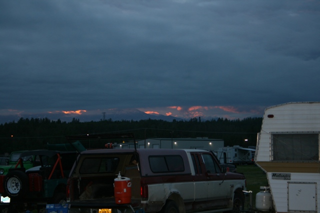 Pickup truck with camper shell parked next to a trailer, with mountains in the background at dusk
