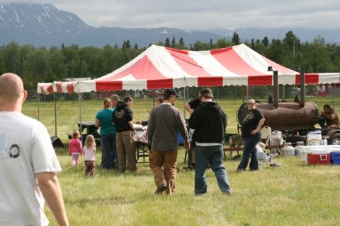 1990 Chevrolet Suburban - An outdoor gathering takes place under a large tent with smokers visible in the background.
