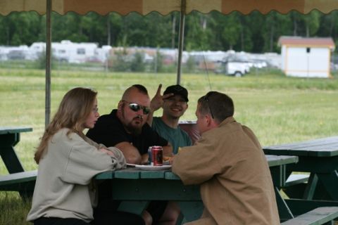 1990 Chevrolet Suburban - A group of people are seated at picnic tables in an outdoor setting, with trees and buildings in the background.