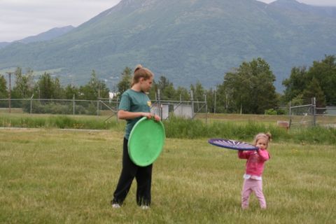 1990 Chevrolet Suburban - Two girls enjoy a game of frisbee in a grassy field with mountains in the distance.
