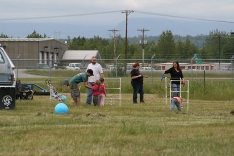 1990 Chevrolet Suburban - A group of people gather in a grassy field near a fence and buildings.