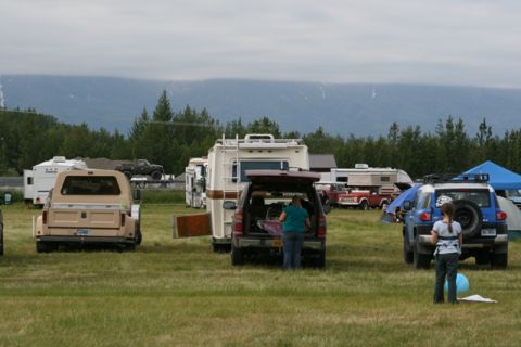 1990 Chevrolet Suburban - A tan pickup truck with a camper shell is parked in a field alongside RVs and other vehicles, with mountains visible in the distance.