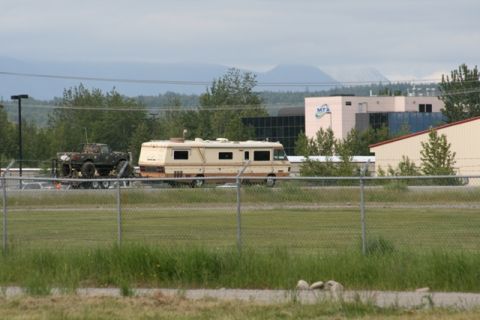 1990 Chevrolet Suburban - An RV is seen towing a modified pickup truck on a trailer, with buildings and mountains in the distance.