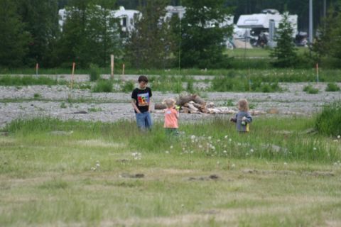 1990 Chevrolet Suburban - Children play in a field near parked RVs, with a pile of firewood visible.