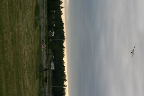 1990 Chevrolet Suburban - A kite soars in the sky above a park with people and trees in the background.