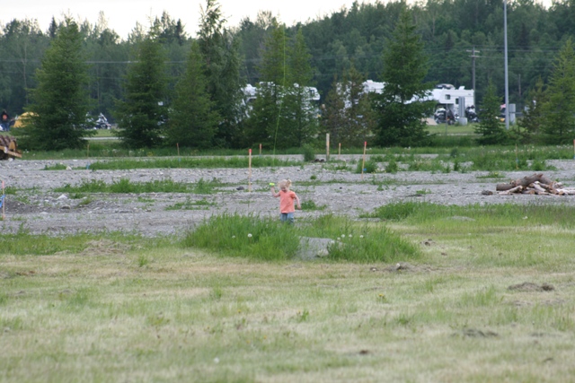 Child playing in a grassy field with RVs and trees in the background