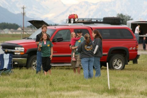 1990 Chevrolet Suburban - A group of people stand around a red pickup truck with a camper shell in a grassy field.