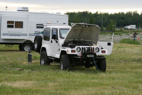 1990 Chevrolet Suburban - A white Jeep Wrangler sits in a grassy field with its hood and driver's door open, revealing the engine compartment.