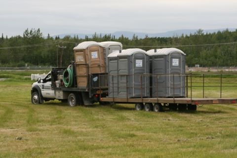 1990 Chevrolet Suburban - A flatbed truck transports multiple portable toilets on a trailer across a grassy field.