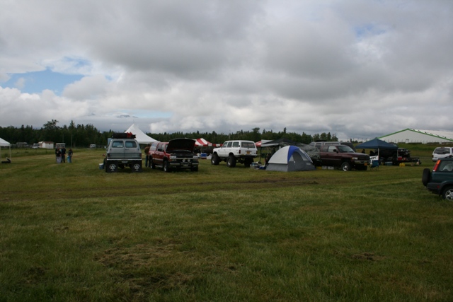 Several SUVs and trucks parked in a field with tents