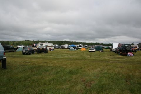 1990 Chevrolet Suburban - A wide view of an outdoor event numerous vehicles, RVs, and tents spread across a grassy field under an overcast sky.