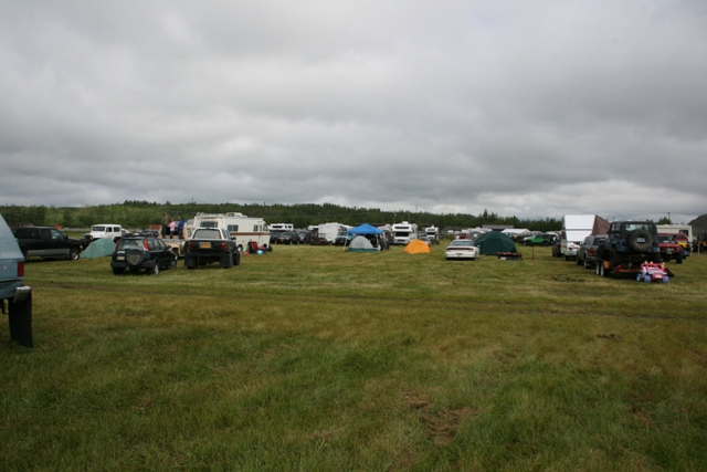 Outdoor gathering with RVs, tents, and various vehicles under a cloudy sky