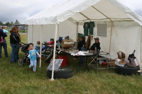 1990 Chevrolet Suburban - An outdoor gathering under a tent features people browsing items on tables, with children present in the foreground and background.