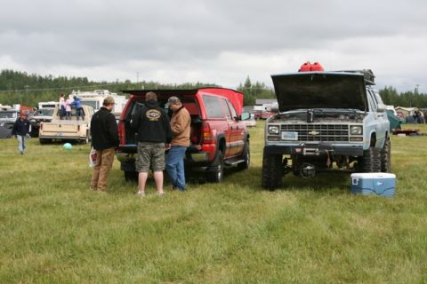 1990 Chevrolet Suburban - A lifted pickup truck with its hood open sits in a grassy field next to another vehicle.