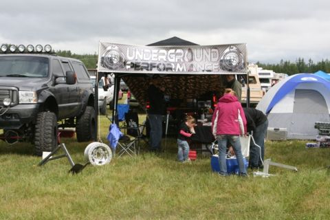 1990 Chevrolet Suburban - A heavily modified SUV is displayed at an outdoor event with a vendor tent and other vehicles in the background.