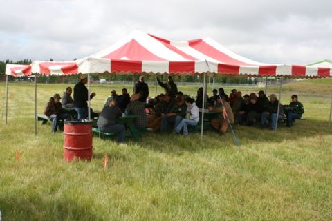 1990 Chevrolet Suburban - An outdoor gathering takes place under a large red and white striped tent with people seated at picnic tables.