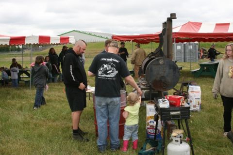 1990 Chevrolet Suburban - An outdoor event features a large barbecue smoker, tents, and people mingling in a grassy area.
