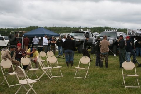 1990 Chevrolet Suburban - A gathering of people and several large, modified trucks are present in an outdoor setting with a blue tent and folding chairs.