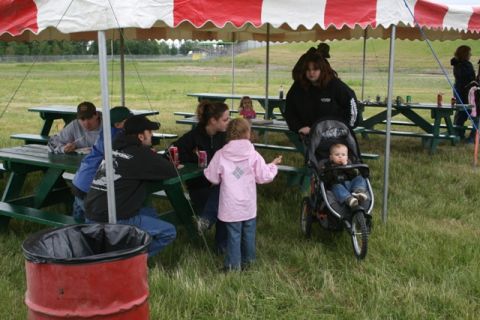 1990 Chevrolet Suburban - An outdoor gathering with people seated at picnic tables under a large tent, with a baby in a stroller nearby.