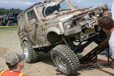 1990 Chevrolet Suburban - An off-road vehicle is being maneuvered up a ramp, covered in mud, with another vehicle visible in the background.