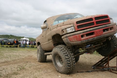 1990 Chevrolet Suburban - A heavily muddied red pickup truck is positioned on a metal ramp during an off-road event.