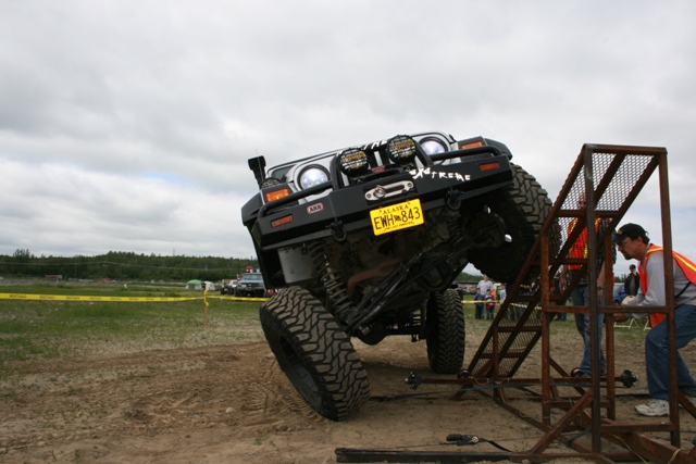 Modified Jeep Wrangler with large tires climbing a metal ramp, "XTREME" text on bumper, Alaska license plate EWH-843