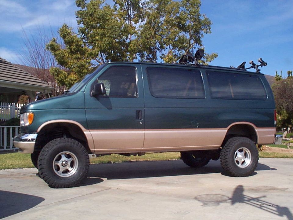 Side view of a lifted 2001 Ford E150 van, green with tan lower body, on a paved surface