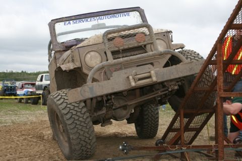 1990 Chevrolet Suburban - A heavily mud-covered off-road vehicle is positioned on a ramp, with other vehicles visible in the background.