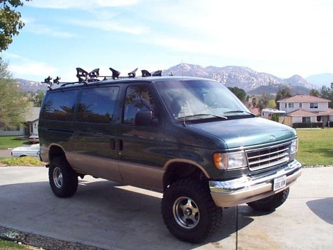 2001 Ford E150 - A modified Ford E-Series van sits parked in a driveway with mountains in the background.