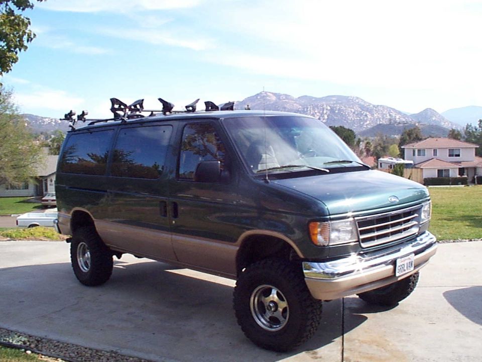 Green Ford E-Series van with off-road tires and roof rack with lights