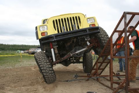 1990 Chevrolet Suburban - A modified yellow jeep is climbing a metal ramp during an off-road event.