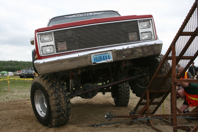 Red lifted 1987 Chevrolet K5 Blazer with chrome grille and large off-road tires, angled up a metal ramp
