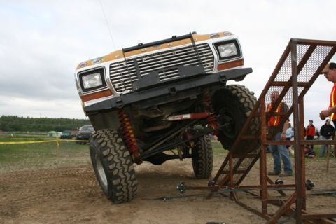 1990 Chevrolet Suburban - A lifted, orange and white Ford truck is angled precariously on a metal ramp structure. The truck's large, knobby tires and suspension are…