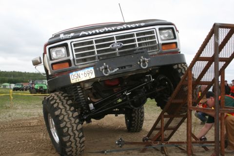 1990 Chevrolet Suburban - A heavily modified, lifted Ford truck with large off-road tires is positioned on a metal ramp, with its front end angled upwards. The truck…