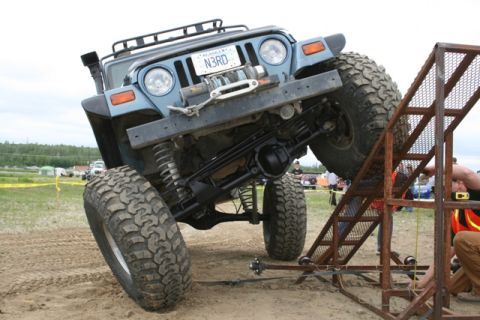 1990 Chevrolet Suburban - A lifted blue Jeep Wrangler is angled up a metal ramp with large off-road tires. The vehicle has a winch on the front bumper and an "N3RD"…