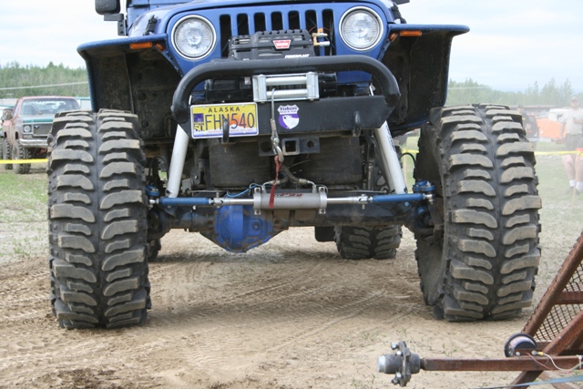 Close-up of the front axle and large tires of a lifted blue Jeep Wrangler with a winch.