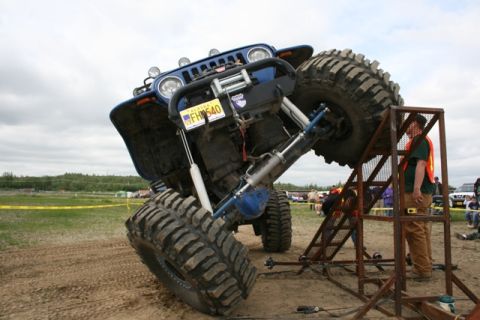 1990 Chevrolet Suburban - A heavily modified blue Jeep Wrangler with oversized tires is tilted on a metal ramp, with a person in an orange safety vest standing nearb…