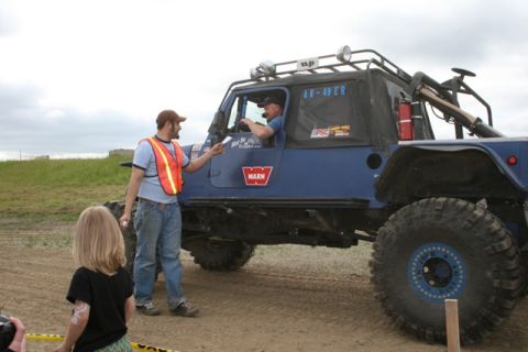 1990 Chevrolet Suburban - A man in an orange safety vest hands a paper to the driver of a blue Jeep Wrangler with large off-road tires and a roof rack. A young child…