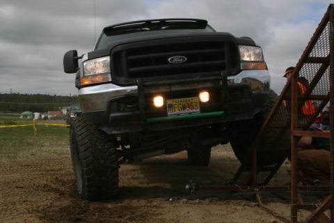 1990 Chevrolet Suburban - A lifted, black Ford Super Duty truck is positioned on a dirt track, with its front end angled towards a metal ramp. The truck features lar…