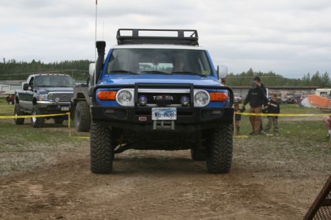 1990 Chevrolet Suburban - A blue Toyota FJ Cruiser with a snorkel and roof rack is parked on a dirt track, facing the camera. A dark colored pickup truck is visible…