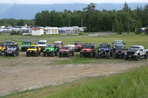 1990 Chevrolet Suburban - A line of modified off-road vehicles, including Jeeps and trucks, are parked on a dirt lot with a wooded area and mountains in the backgrou…