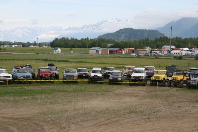 Off-road vehicles parked in a field with mountains in the background.