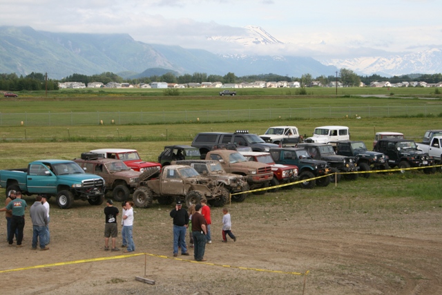 Off-road vehicles parked in a dirt lot with people standing around.