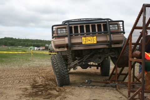 1990 Chevrolet Suburban - A lifted, tan Jeep Cherokee with an aftermarket brush guard and yellow Alaska license plate is positioned on a sandy track next to a metal…