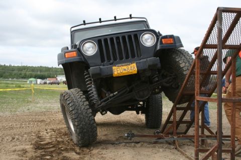 1990 Chevrolet Suburban - A black Jeep Wrangler is angled steeply on a sandy surface, with its front tire resting on a metal ramp. The vehicle is positioned as if pe…