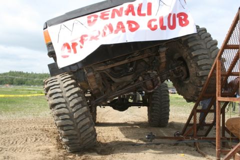 1990 Chevrolet Suburban - A heavily modified off-road truck with oversized tires is shown at an extreme angle, climbing a ramp. A banner on the truck reads "DENALI O…